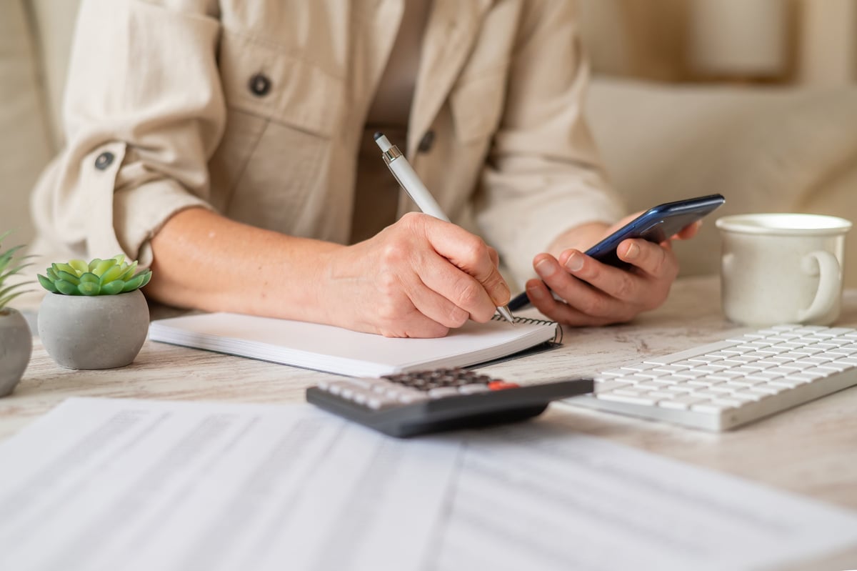 Hands writing notes in a notebook while managing personal finances